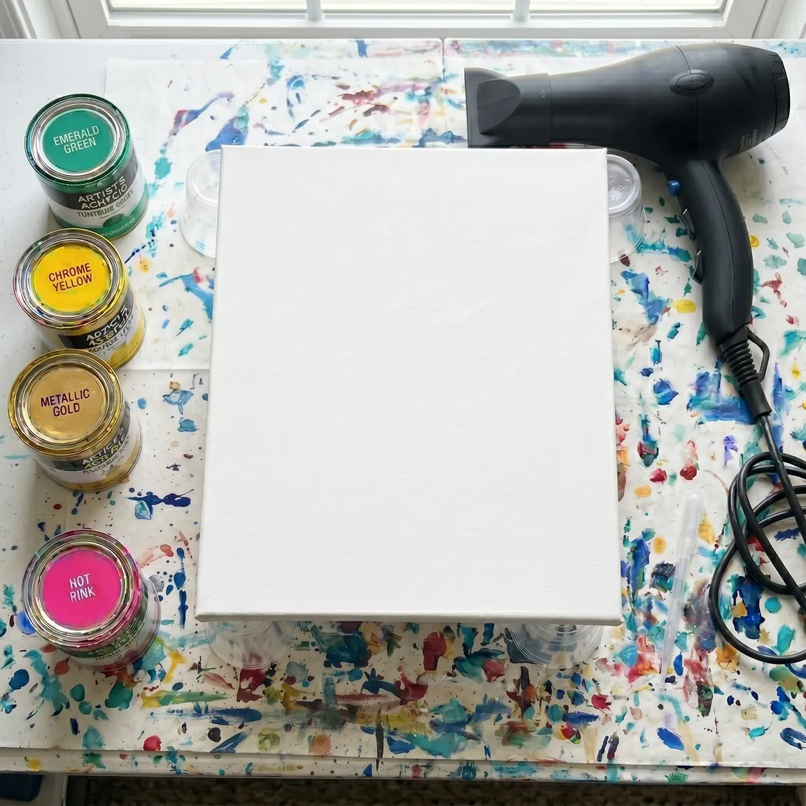 Workspace with paints, canvas, and hairdryer